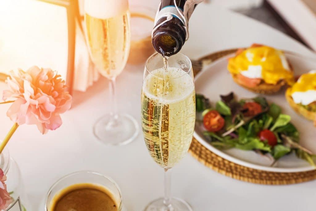 Someone pouring some prosecco with their breakfast food at a bottomless brunch in London