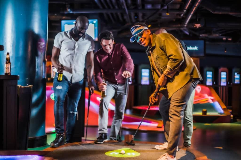 four people enjoying a game of mini golf at an indoor putt putt golf arena